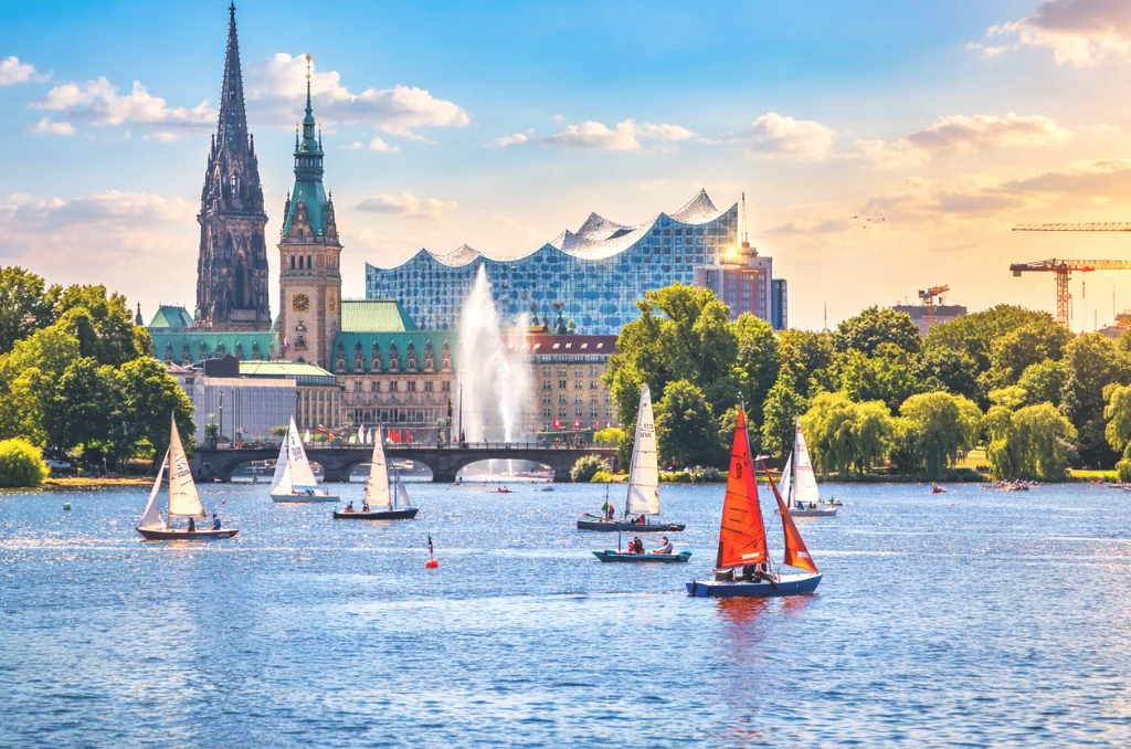 Ein sonniger Tag auf der Hamburger Außenalster mit Segelbooten und der berühmten Skyline im Hintergrund, inklusive Elbphilharmonie und Rathaus. Ein sonniger Tag auf der Hamburger Außenalster mit Segelbooten und der berühmten Skyline im Hintergrund, inklusive Elbphilharmonie und Rathaus.